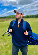Man holding a golf bag on a golf course with a blue sky and clouds in the background